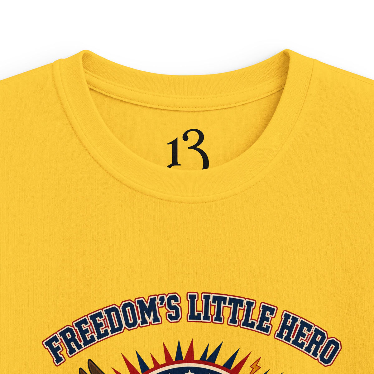 Close-up of yellow kids T-shirt neckline and “Freedom’s Little Hero” graphic.